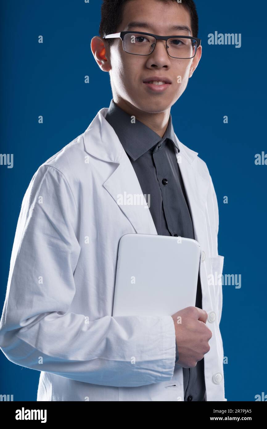 Jeune chercheur asiatique avec une tablette numérique, portant un manteau blanc sur une chemise gris foncé. Plus de dossiers papier dans les pays civilisés, grâce à Banque D'Images