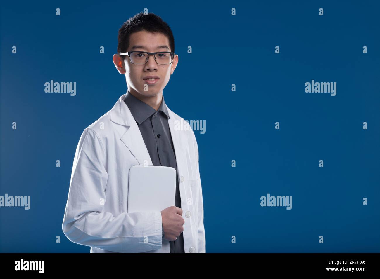 Chercheur asiatique utilisant une tablette numérique, vêtu d'une blouse de laboratoire blanche et d'une chemise gris foncé. Dans les pays avancés, les informations sans fin sont portables pour Banque D'Images