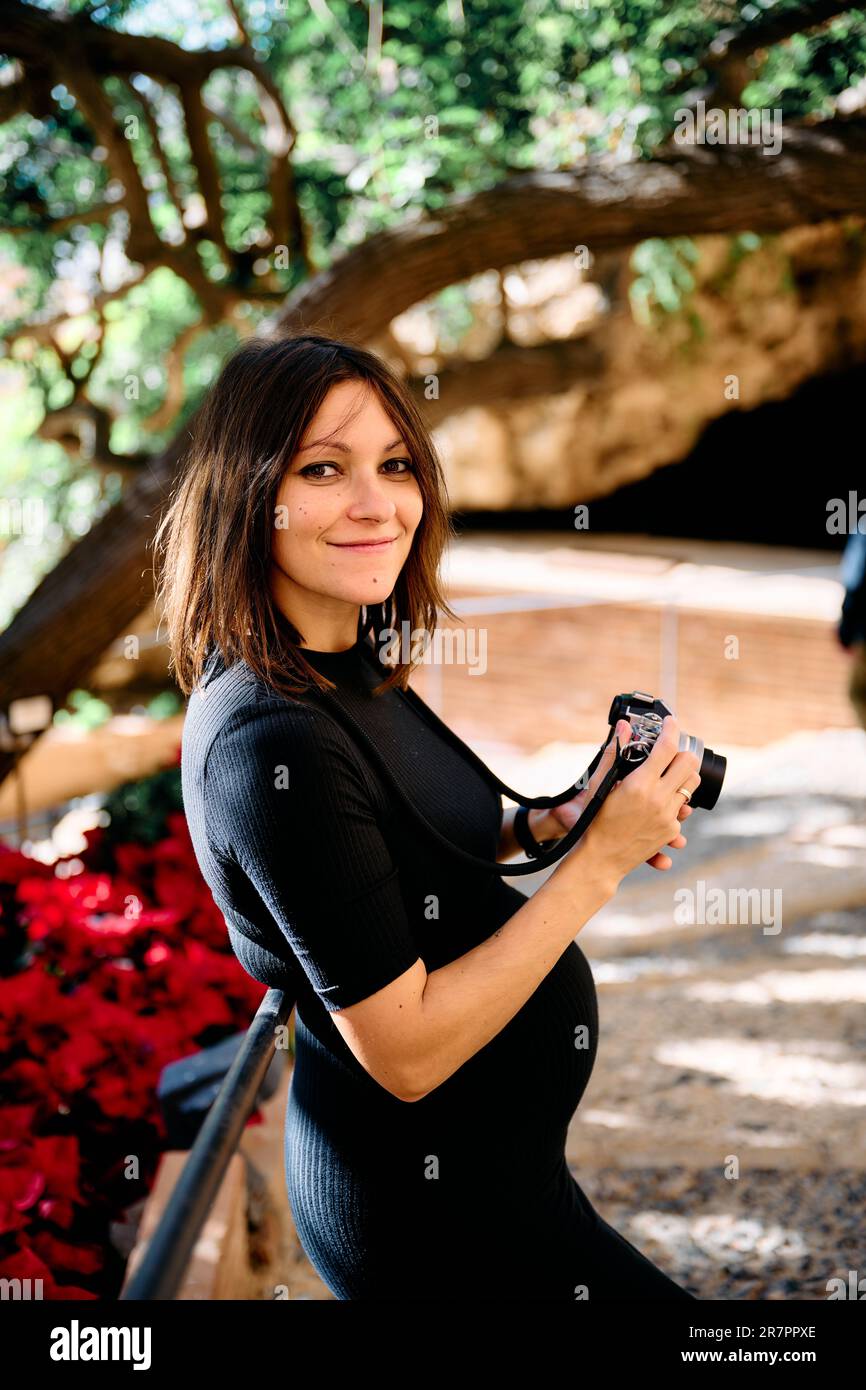 portrait d'une jeune femme dans une robe serrée au cours de ses premiers mois de grossesse prenant des photos avec un appareil-photo ancien et regardant l'appareil-photo. Banque D'Images