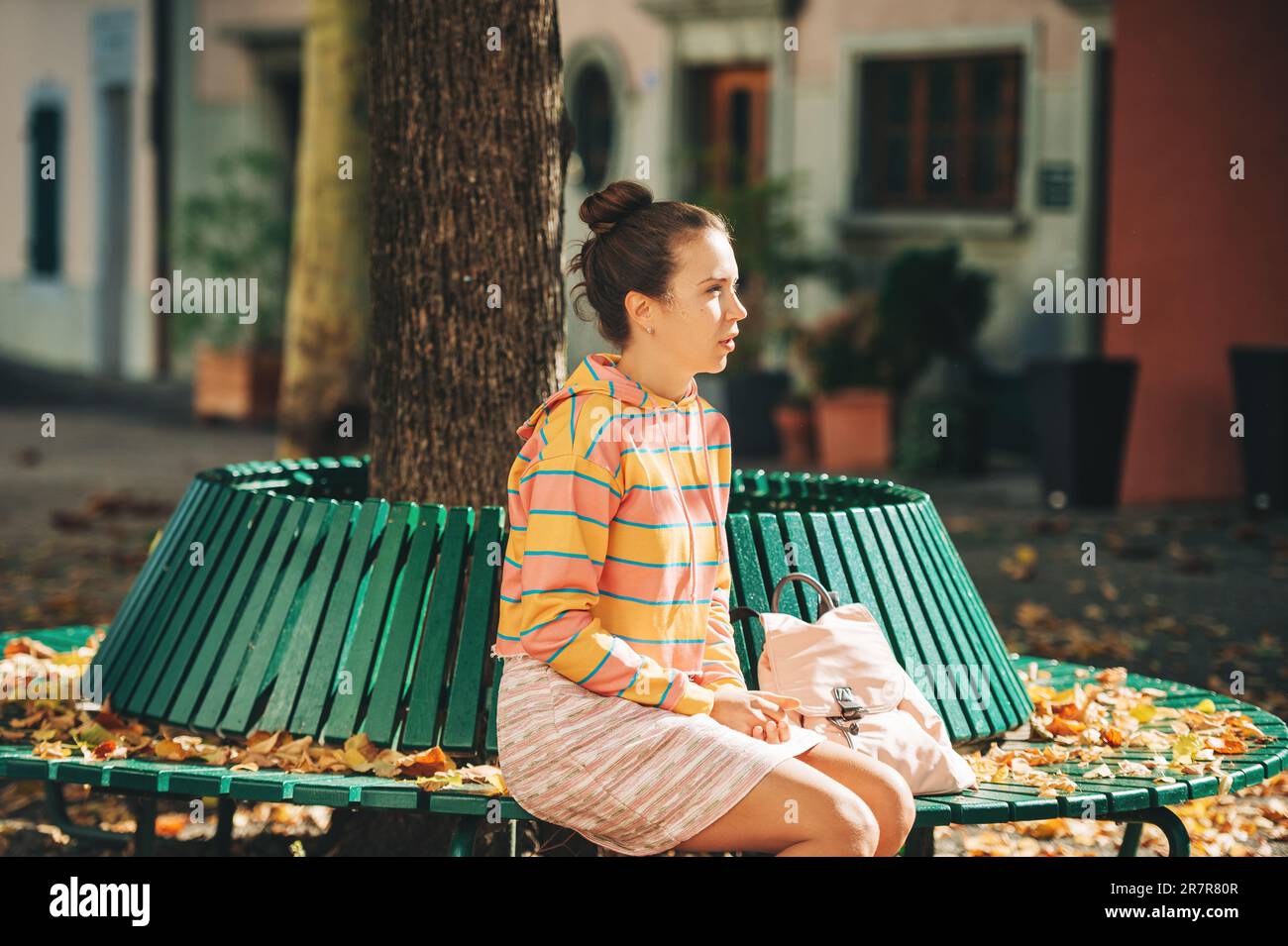 Portrait d'automne de jeune belle femme assise sur le banc à la lumière du soleil, portant un sweat-shirt rayé et une mini jupe Banque D'Images