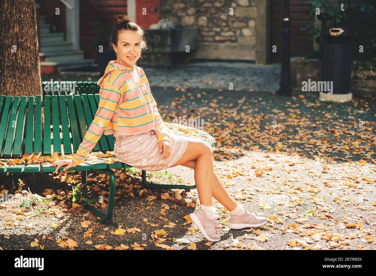 Portrait d'automne de jeune belle femme assise sur le banc à la lumière du soleil, portant un sweat-shirt rayé et une mini jupe Banque D'Images