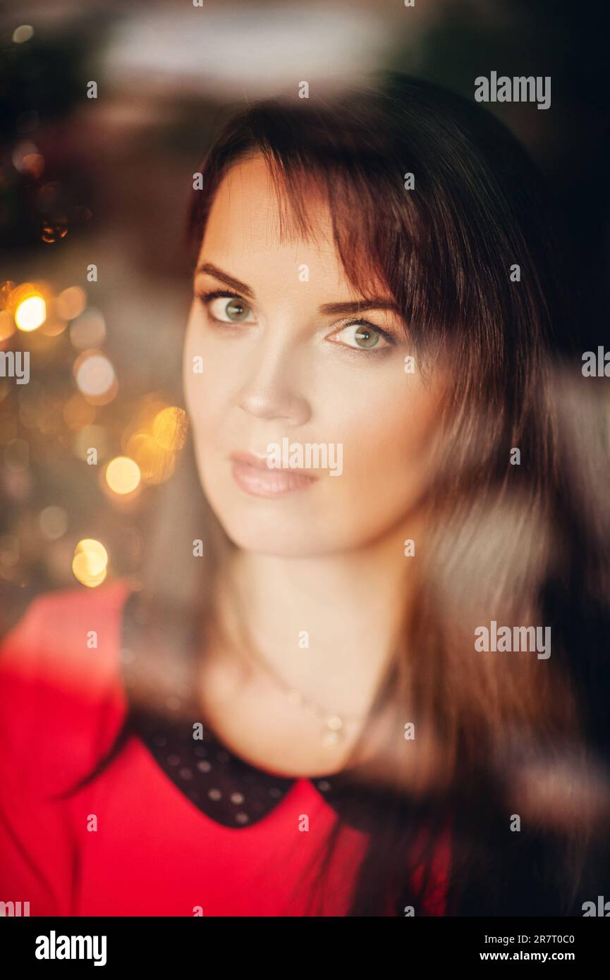 Portrait de Noël de la belle femme aux cheveux foncés, portant une robe rouge, image prise par la fenêtre Banque D'Images