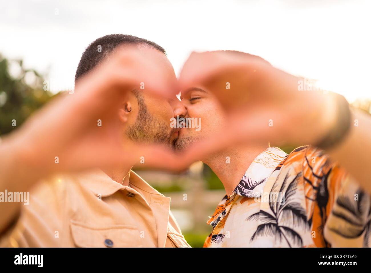 Portrait d'un petit ami gay et d'une petite amie faisant le coeur ou l'amour gestuelle embrassant au coucher du soleil dans un parc de la ville. Diversité et concept lgbt Banque D'Images