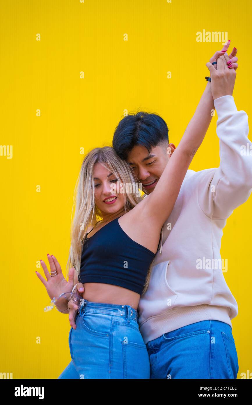 Danse multiethnique d'un couple asiatique et caucasien dansant le bachata sur fond jaune Banque D'Images