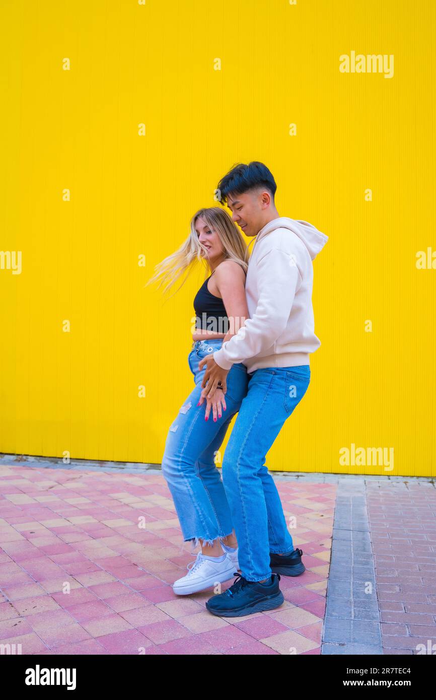 Danse multiethnique d'un couple asiatique et caucasien dansant le bachata sur fond jaune Banque D'Images