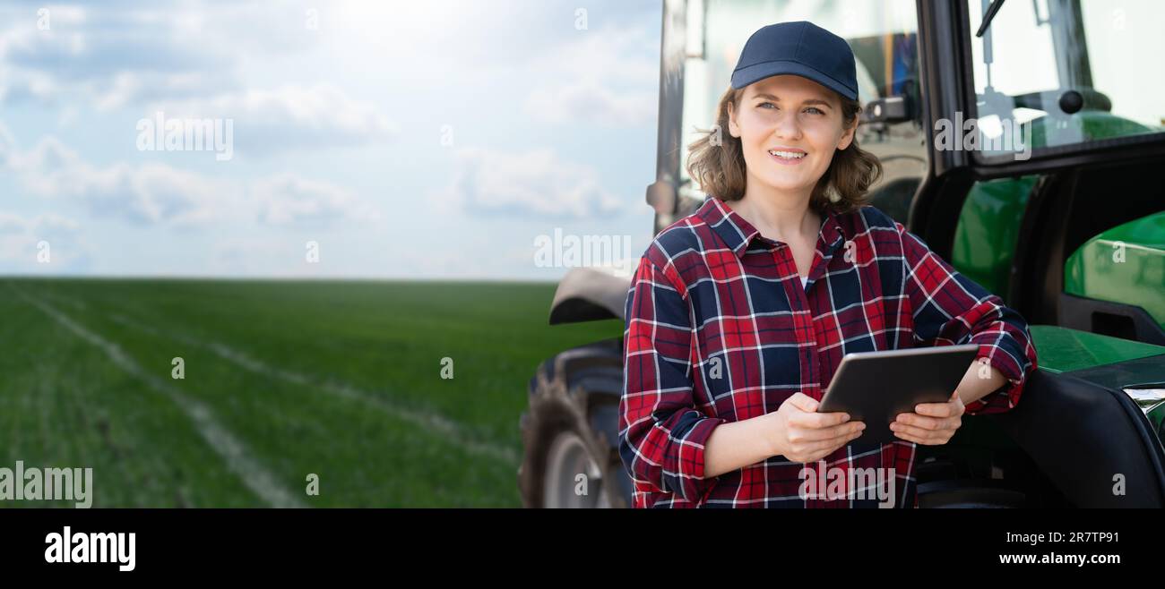 Femme agriculteur avec une tablette numérique à côté d'un tracteur agricole Banque D'Images