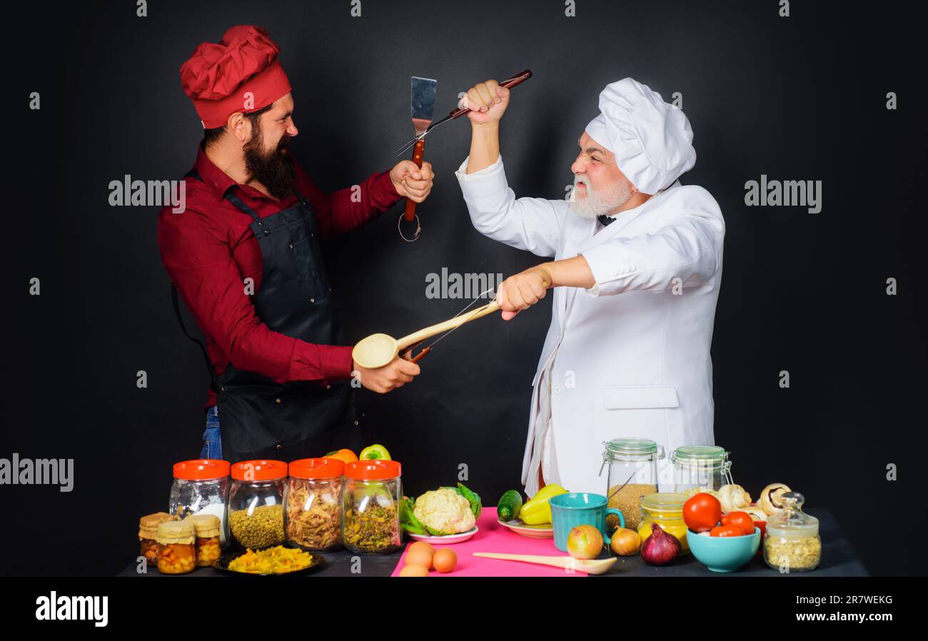 Deux chefs se battent avec des ustensiles de cuisine. Cuisine professionnelle. Les chefs en uniforme participent au spectacle culinaire. Défi de cuisine. Bataille culinaire Banque D'Images