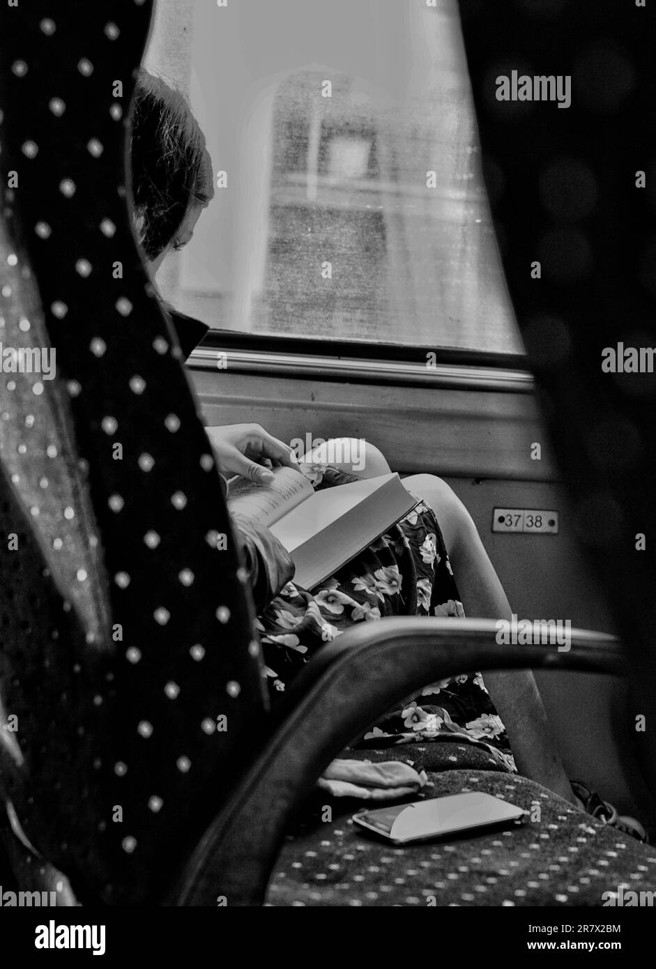 Une jeune femme est vue regardant attentivement un livre alors qu'elle était assise dans un bus sur une image noire et blanche Banque D'Images