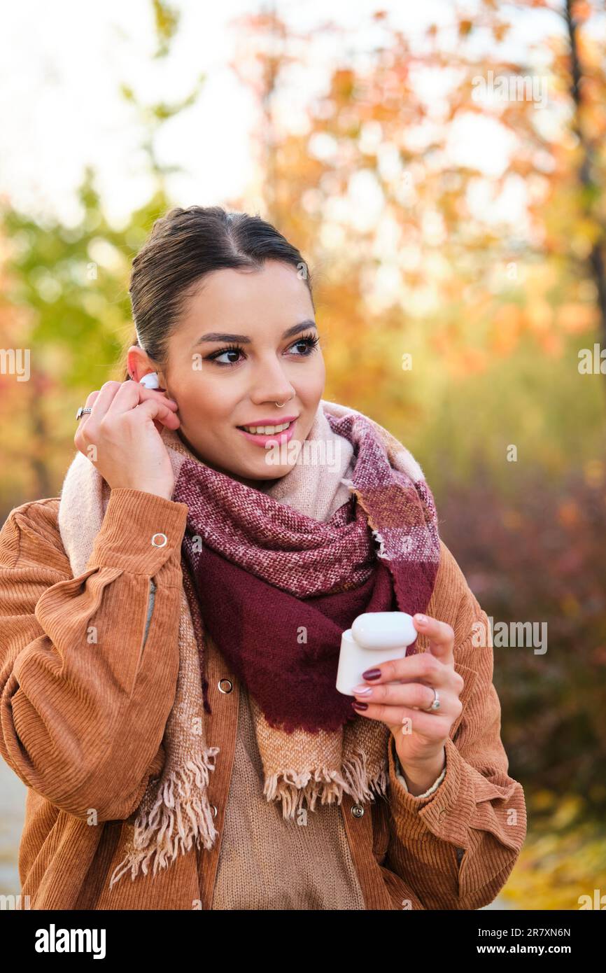 Jeune femme caucasienne portant des écouteurs souriant en automne. Banque D'Images