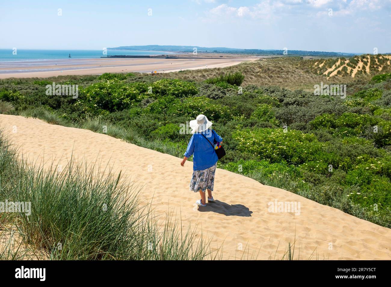 Camber Sands Beach East Sussex , Angleterre , Royaume-Uni - une femme marchant à travers les dunes de sable sur la plage lors d'une belle journée chaude et ensoleillée en été Banque D'Images