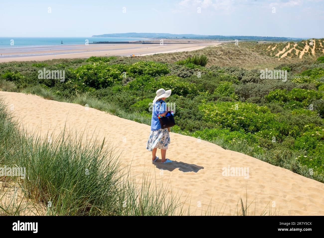 Camber Sands Beach East Sussex , Angleterre , Royaume-Uni - une femme marchant à travers les dunes de sable sur la plage lors d'une belle journée chaude et ensoleillée en été Banque D'Images
