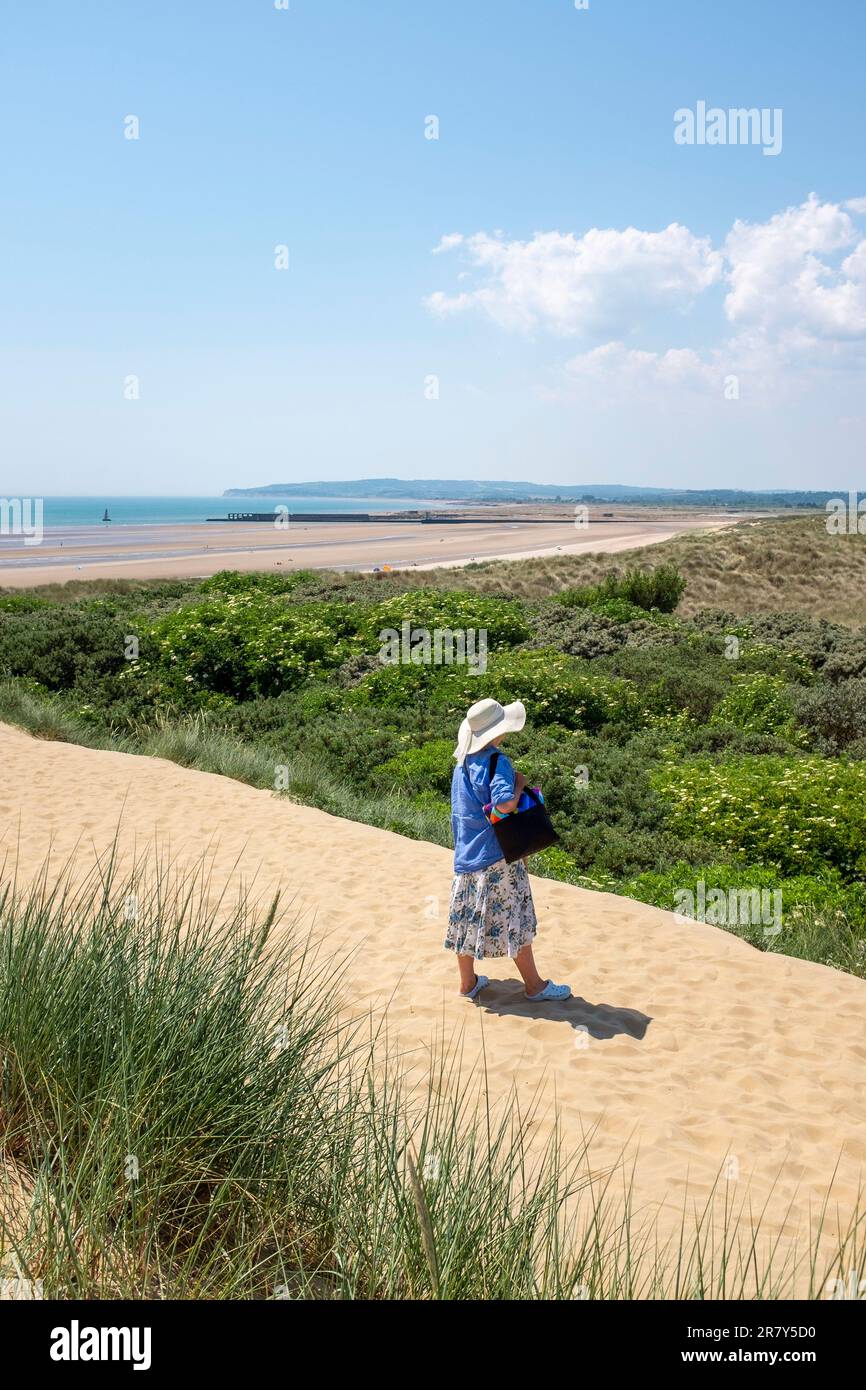 Camber Sands Beach East Sussex , Angleterre , Royaume-Uni - une femme marchant à travers les dunes de sable sur la plage lors d'une belle journée chaude et ensoleillée en été Banque D'Images