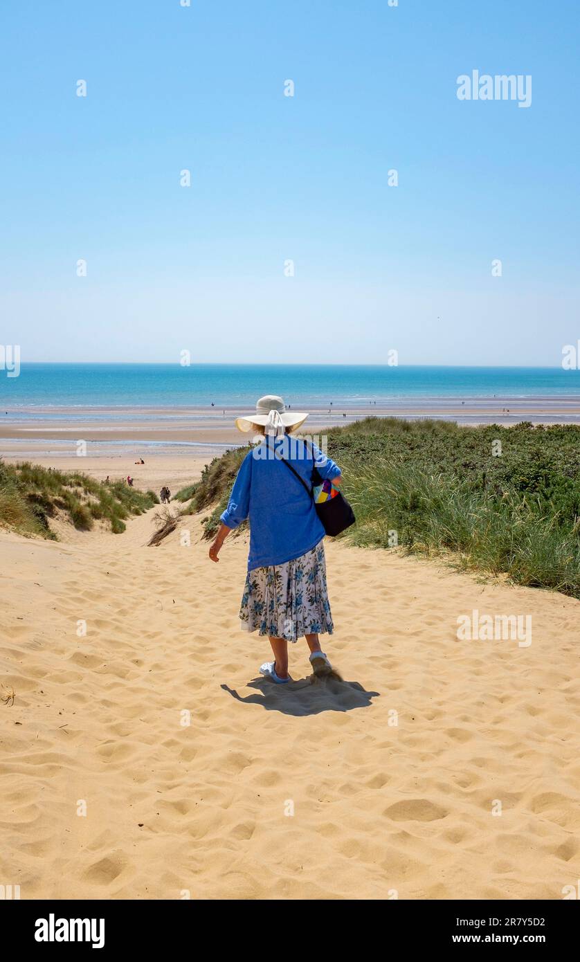 Camber Sands Beach East Sussex , Angleterre , Royaume-Uni - une femme marchant à travers les dunes de sable sur la plage lors d'une belle journée chaude et ensoleillée en été Banque D'Images