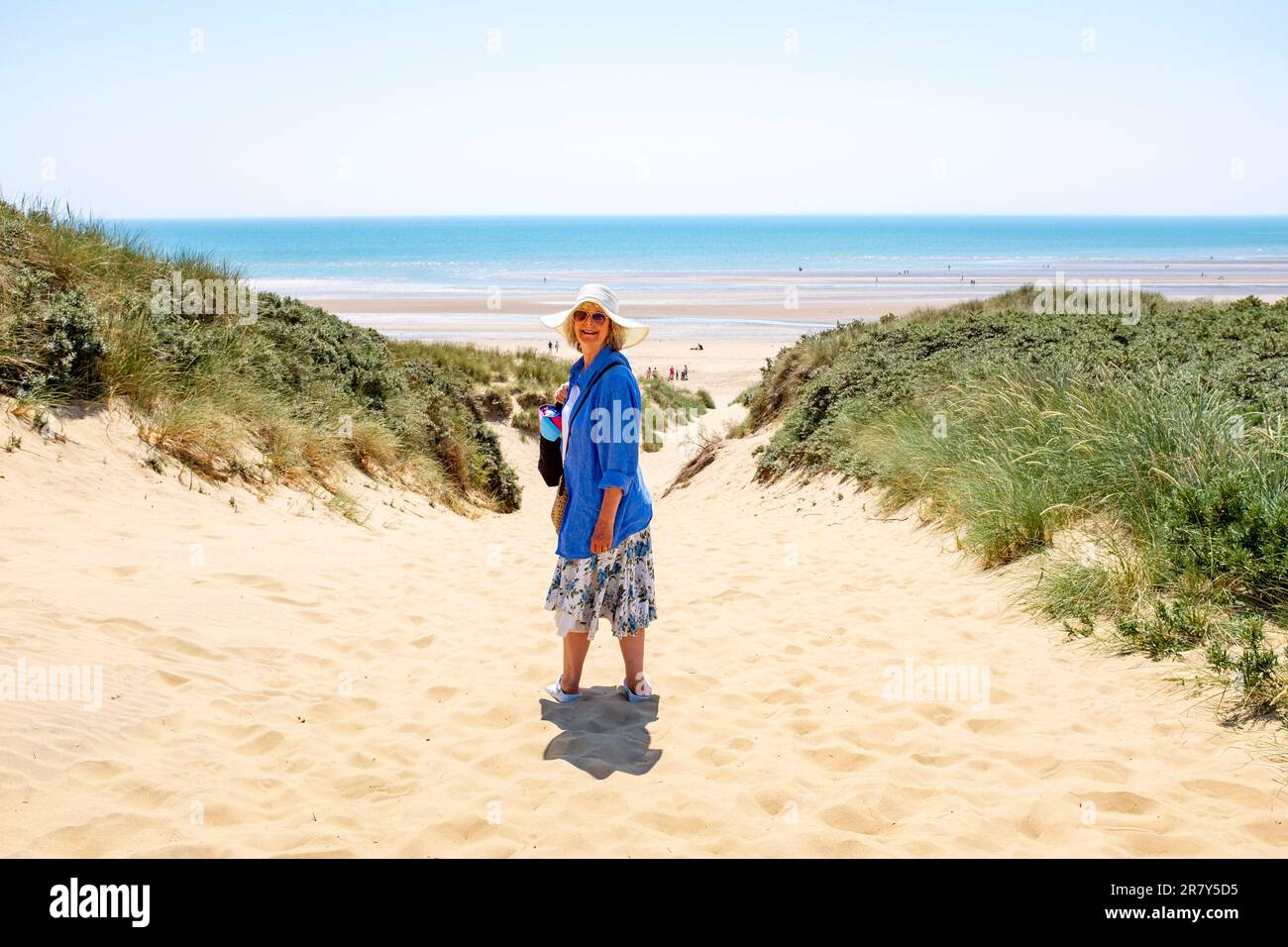Camber Sands Beach East Sussex , Angleterre , Royaume-Uni - une femme marchant à travers les dunes de sable sur la plage lors d'une belle journée chaude et ensoleillée en été Banque D'Images