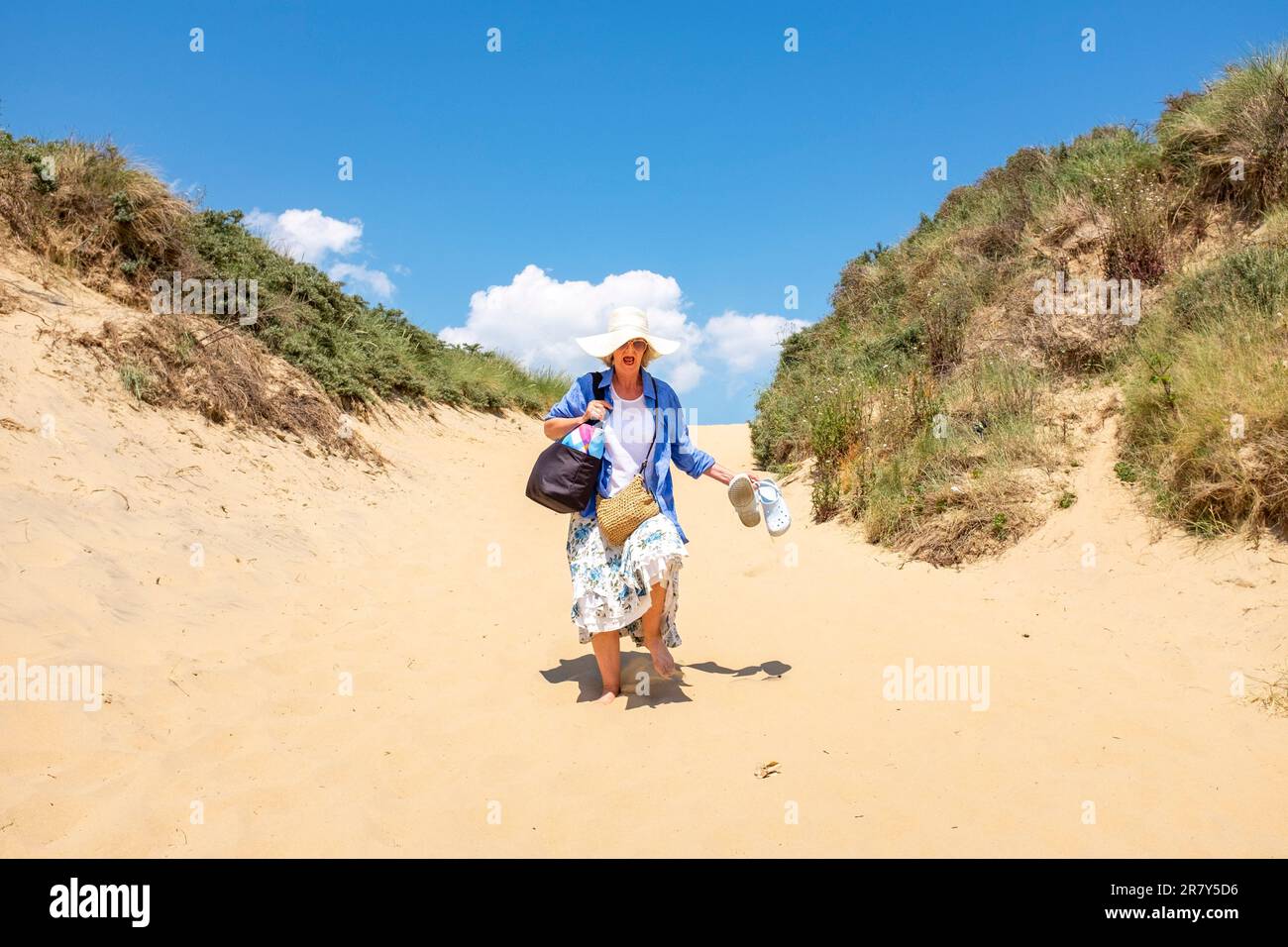 Camber Sands Beach East Sussex , Angleterre , Royaume-Uni - une femme qui se promène à travers les dunes de sable chaud sur la plage lors d'une belle journée chaude et ensoleillée en été Banque D'Images