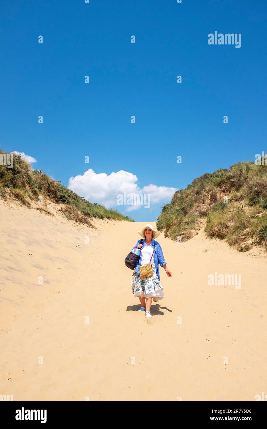 Camber Sands Beach East Sussex , Angleterre , Royaume-Uni - une femme marchant à travers les dunes de sable sur la plage lors d'une belle journée chaude et ensoleillée en été Banque D'Images