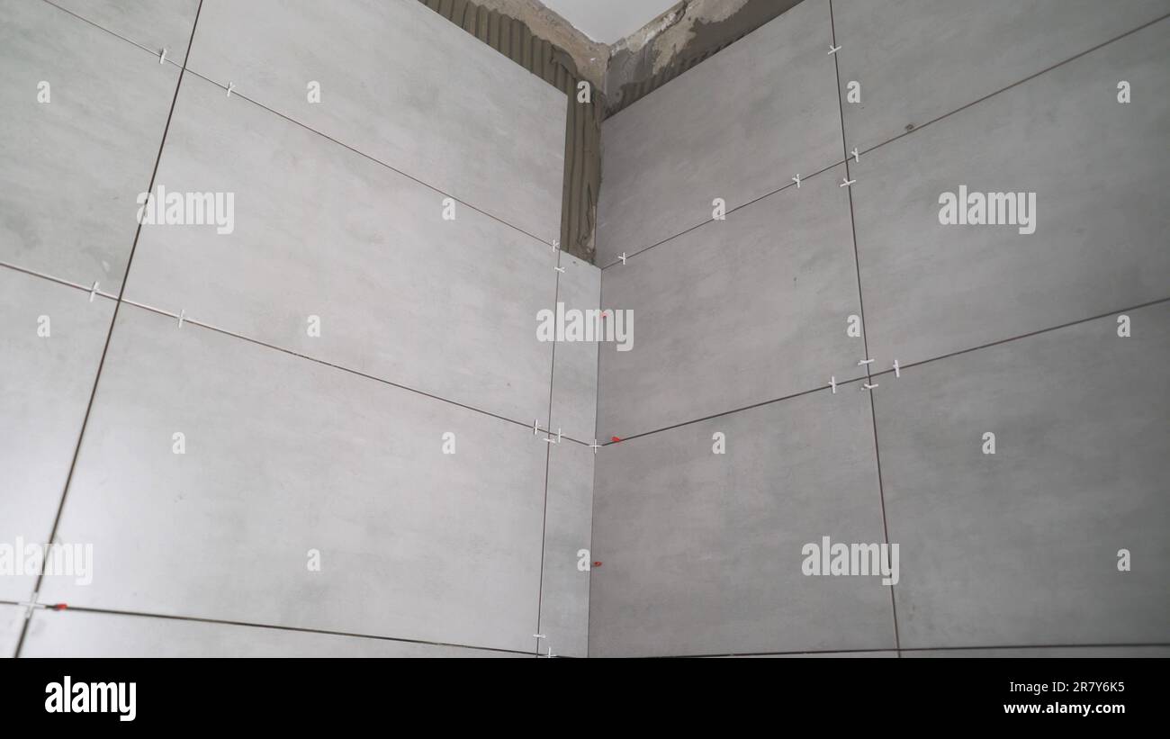 Un ouvrier d'entretien dépose de grands carreaux de céramique sur les murs d'une pièce. Carrelage dans la salle de bains, sur le mur. Carrelage en céramique dans la salle de bains. Banque D'Images
