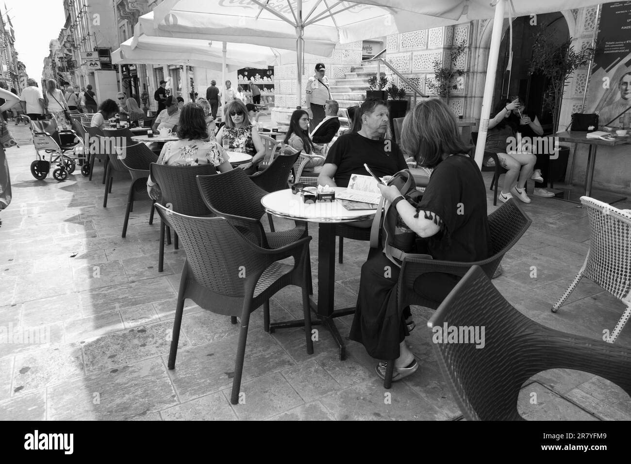 Photographie en noir et blanc d'un café en plein air très fréquenté dans la rue de la République de la Valette, Malte Banque D'Images