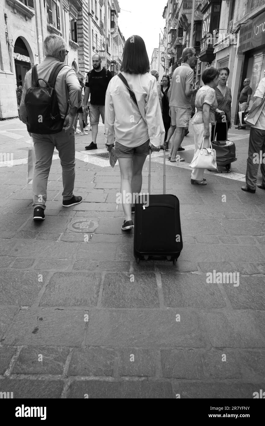 Photographie en noir et blanc de touristes avec sac à dos ou chariot dans la rue de la République de la Valette, Malte Banque D'Images