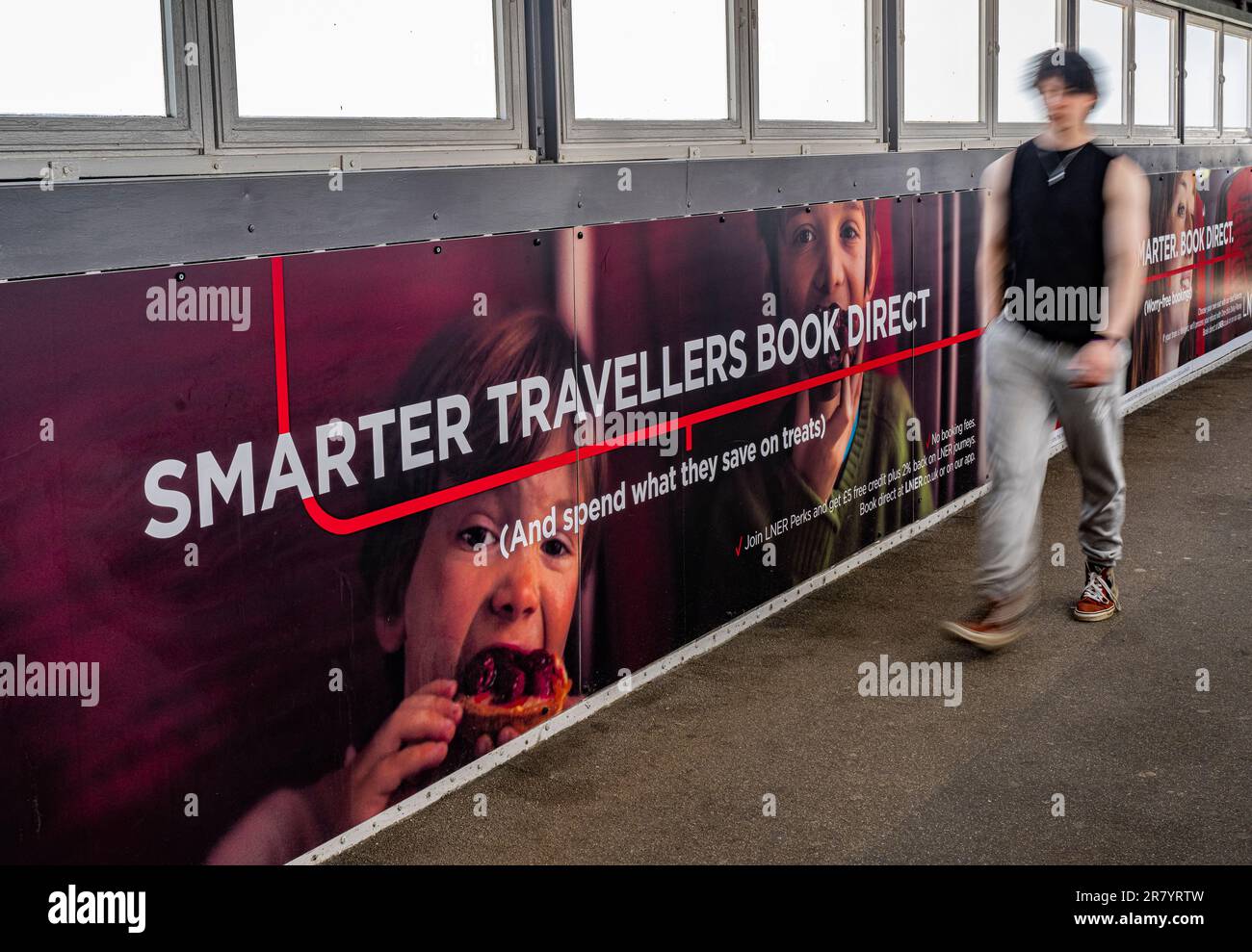 Un jeune homme qui marche devant une arraisonnement publicitaire pour le chemin de fer nord-est de Londres (LNER) pour des voyages plus intelligents et des réservations directes Banque D'Images