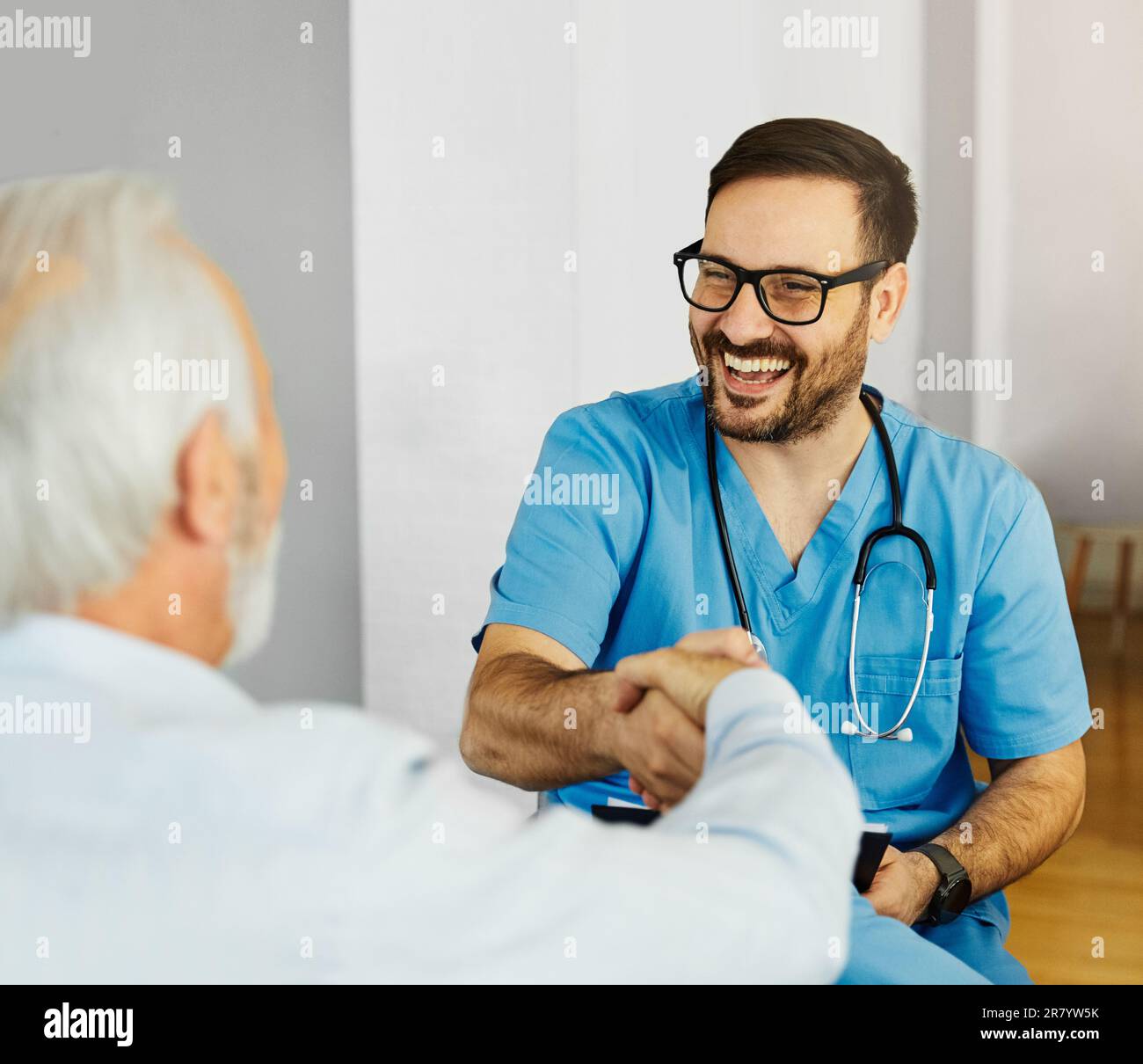 Portrait d'un médecin ou d'un soignant masculin avec un homme âgé qui se secoue les mains à la maison ou à la maison de soins infirmiers Banque D'Images