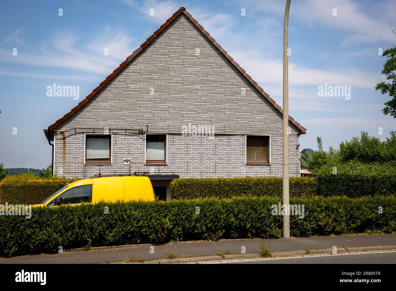 Une voiture jaune se trouve derrière une haie devant une maison en briques grises à Gevelsberg-Silschede, Rhénanie-du-Nord-Westphalie, Allemagne. indication de direction automatique ein gelbes Banque D'Images