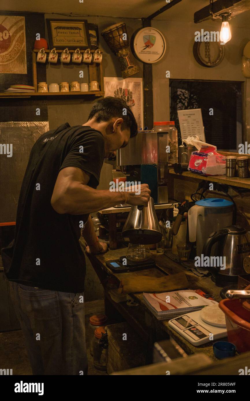 Un barista prépare une tasse de café dans un coffeeshop de la ville de Medan. l'atmosphère de la pièce est sombre avec des lumières faibles. Banque D'Images