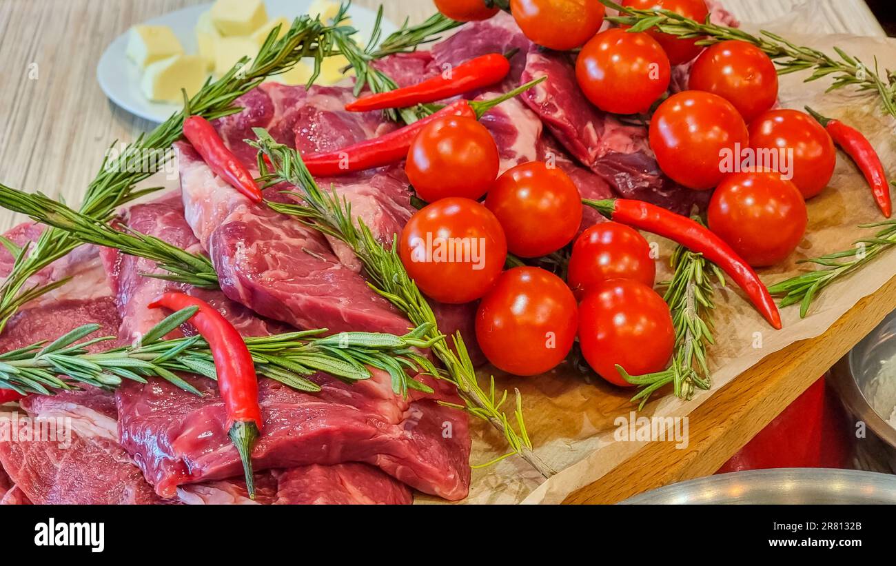 Rouleau de papier d'aluminium avec morceau de viande crue, tomates, romarin et épices sur table en bois de couleur, gros plan Banque D'Images