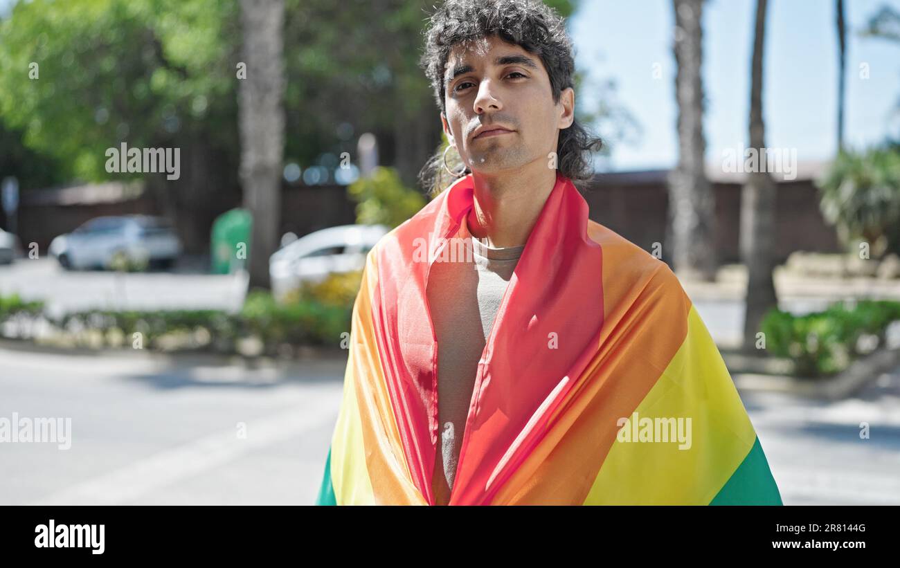 Jeune homme hispanique portant le drapeau arc-en-ciel avec expression détendue dans la rue Banque D'Images