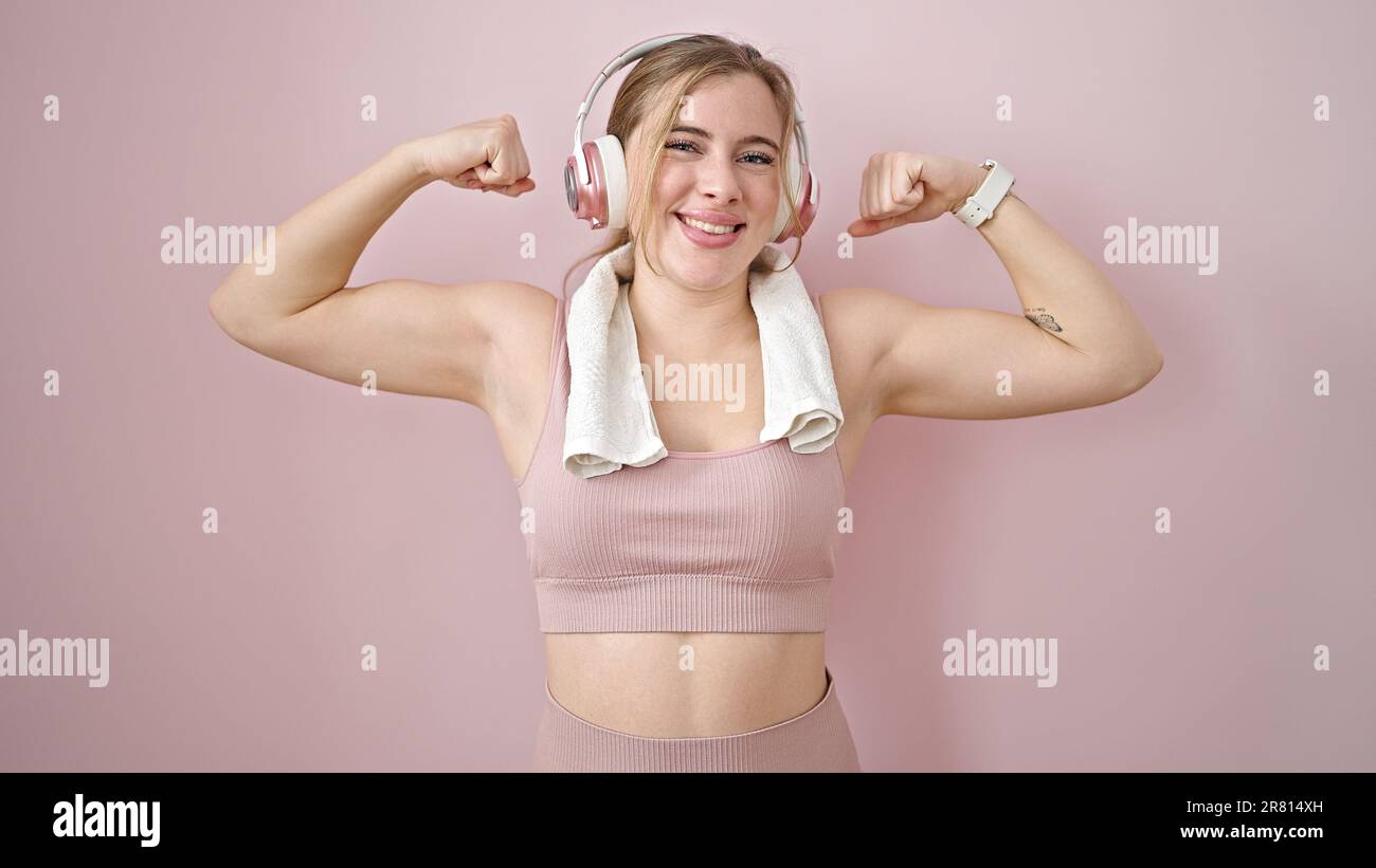 Jeune femme blonde écoutant de la musique faisant un geste fort avec les bras sur fond rose isolé Banque D'Images