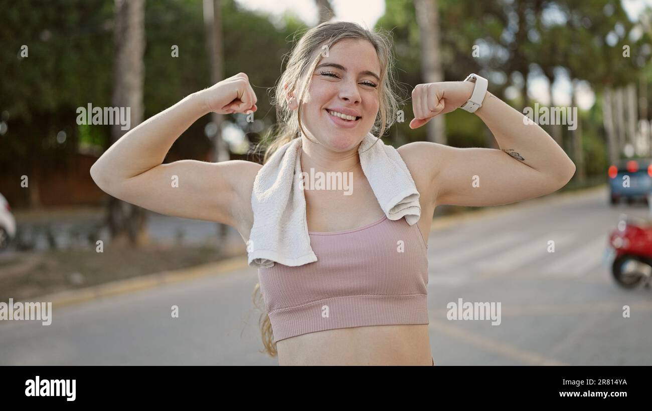Jeune femme blonde portant des vêtements de sport faisant un geste fort avec les bras dans la rue Banque D'Images