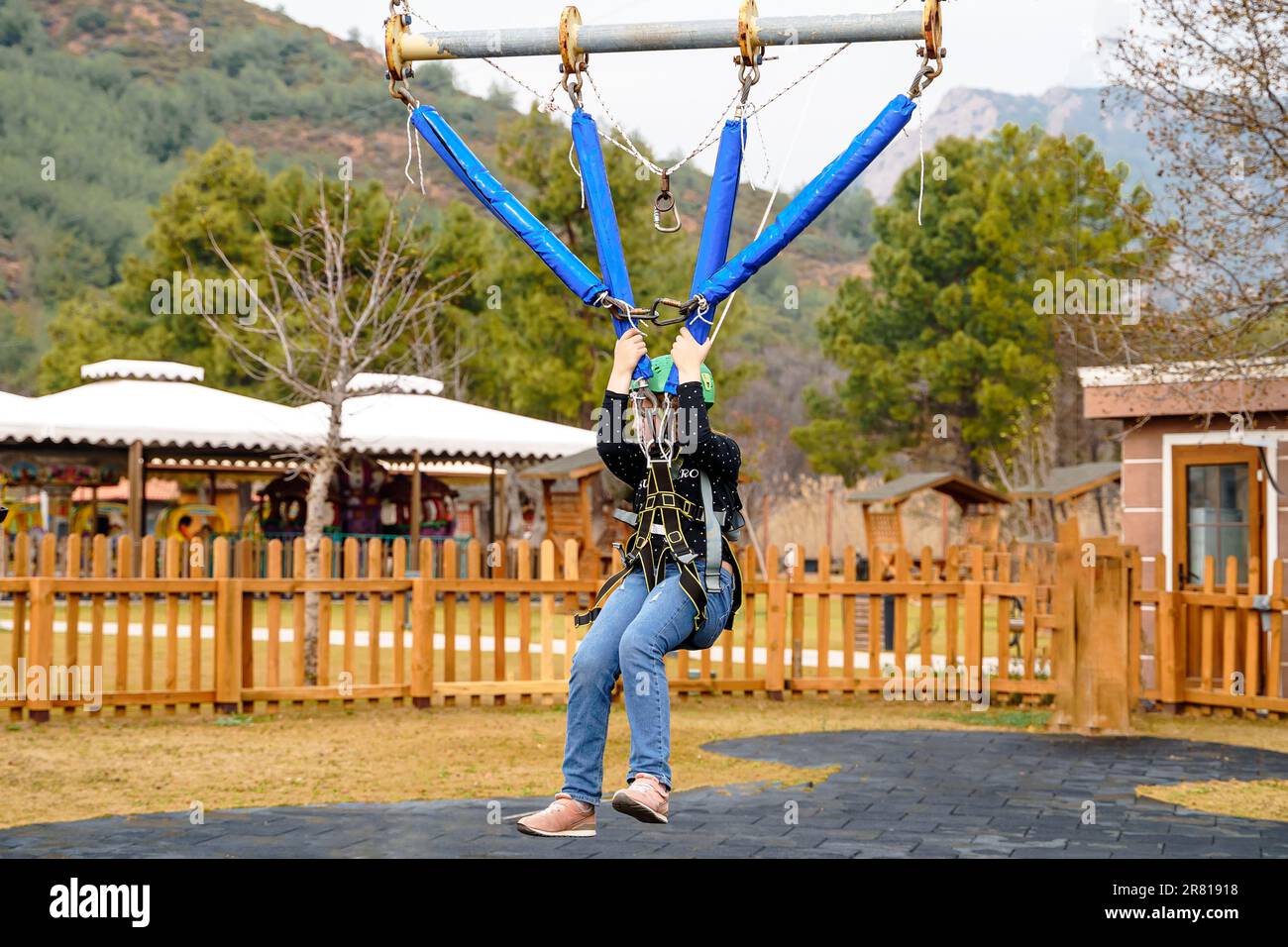 Une adolescente à l'adolescence, un sandow volant dans le parc d'attractions de corde. Équipement de harnais d'escalade, casque de sécurité sport vert. Course d'obstacle suspendu. Enfants enfants Banque D'Images