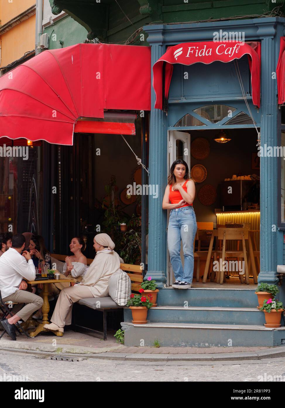 Une serveuse se tient dans la porte d'un café alors que les clients socialisent à l'extérieur dans le quartier coloré de Balat, dans le quartier de Fatih à Istanbul, en Turquie Banque D'Images