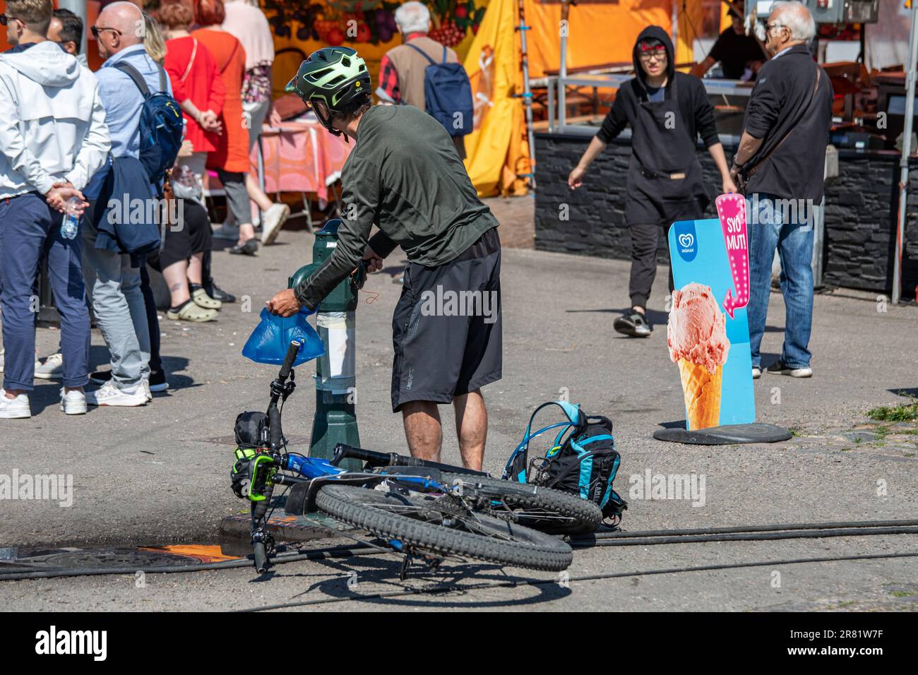 Homme avec un casque de vélo qui remplit un sac d'eau de la fontaine publique de la place du marché à Helsinki, en Finlande Banque D'Images