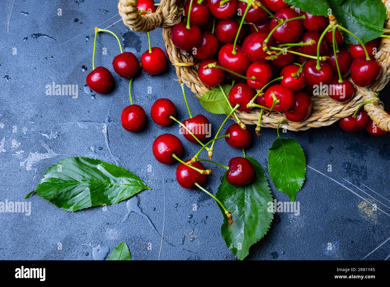 Cerises rouges fraîches, cerises biologiques dans un panier en osier sur fond noir, vue du dessus. Banque D'Images