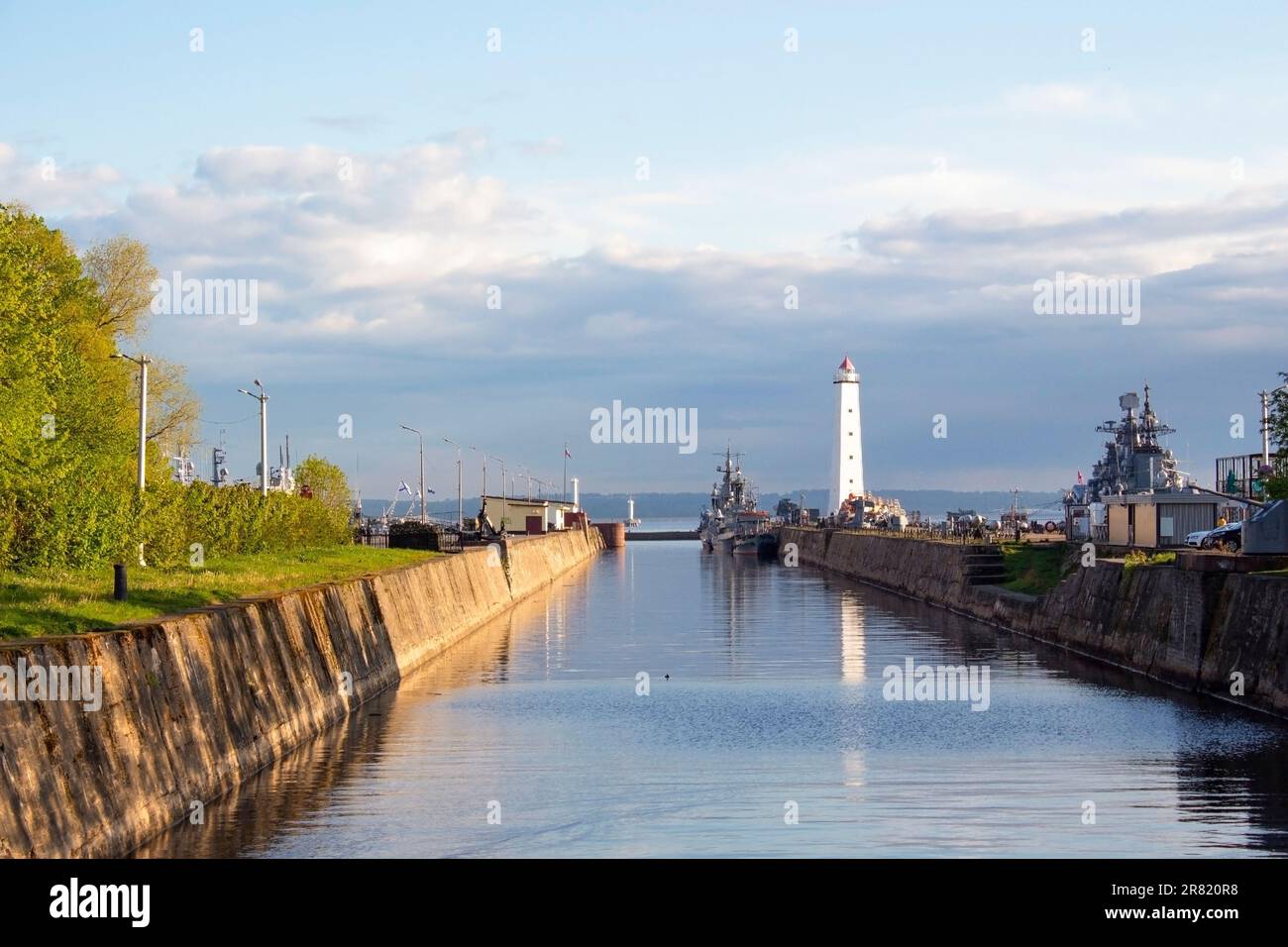 Kronshtadt, Russie. 05.22.2023. Vue sur le canal de Petrovsky, vieux phare en bois blanc et navire de guerre amarré dans le port de Kronstadt. Banque D'Images