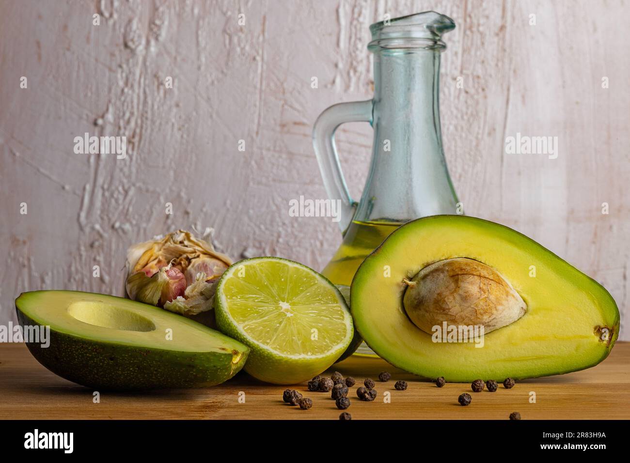 Produits de pâte d'avocat. Avocat, lime, ail, poivre sur une planche de bois. Huile d'olive dans une bouteille transparente en verre. Arrière-plan rustique et lumineux. Cuisine italienne Banque D'Images