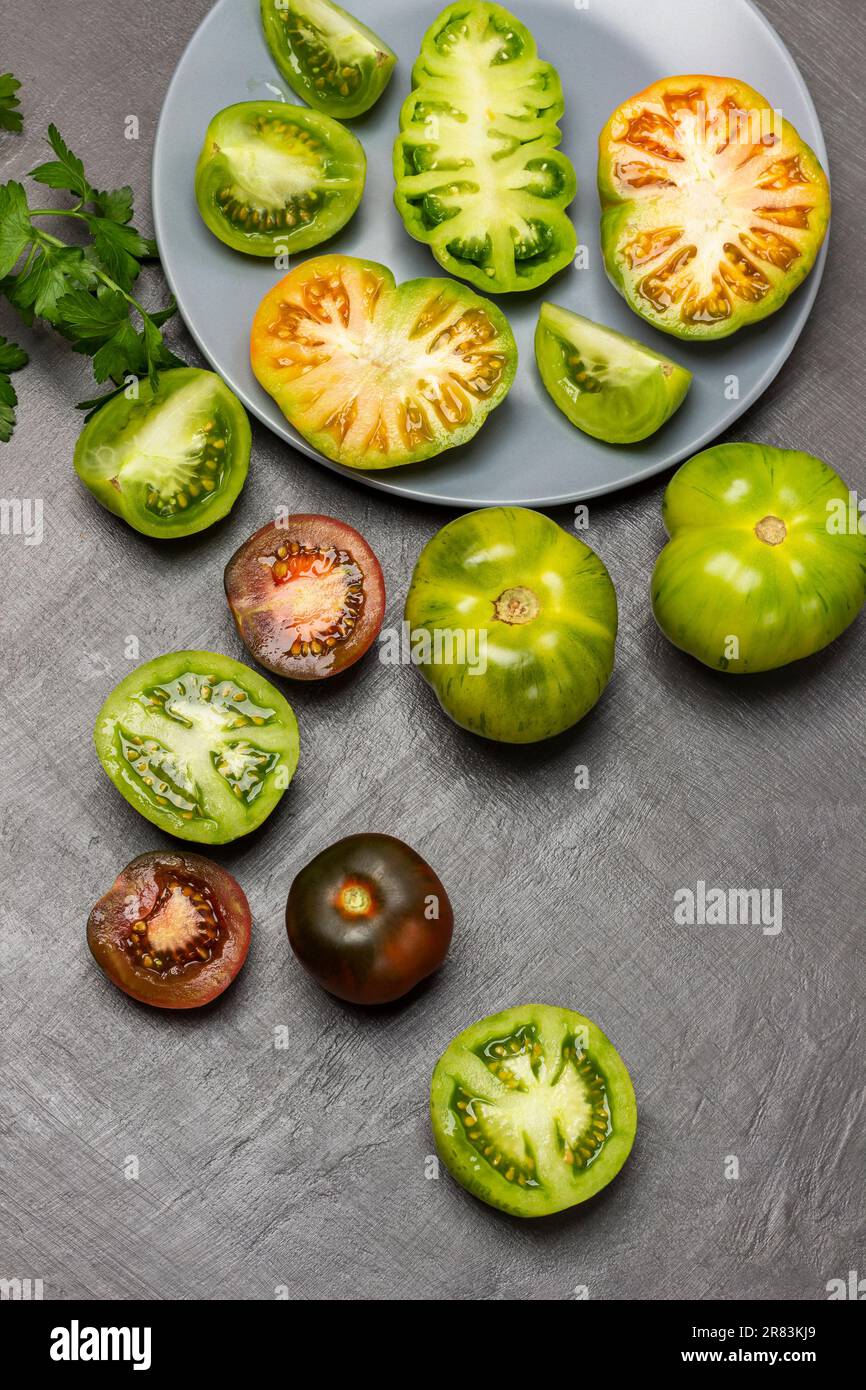 Différentes variétés de tomates vertes et rouges dans une assiette et sur la table. Pose à plat. Arrière-plan gris. Banque D'Images