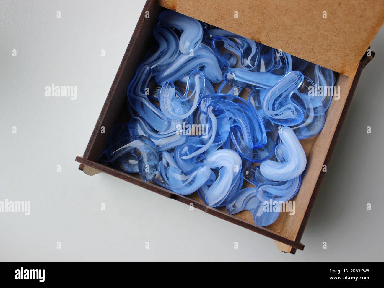 Boîte en contreplaqué avec couvercle ouvert à moitié remplie de pierres cristallines artificielles bleues translucides Banque D'Images
