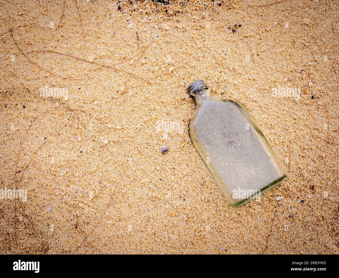 Bouteille plate en verre sur la plage de sable avec espace pour copier, vue de dessus. Gros plan, une bouteille de liqueur usagée vide et sans bouchon, entassées de sable sur la plage. Pollut Banque D'Images