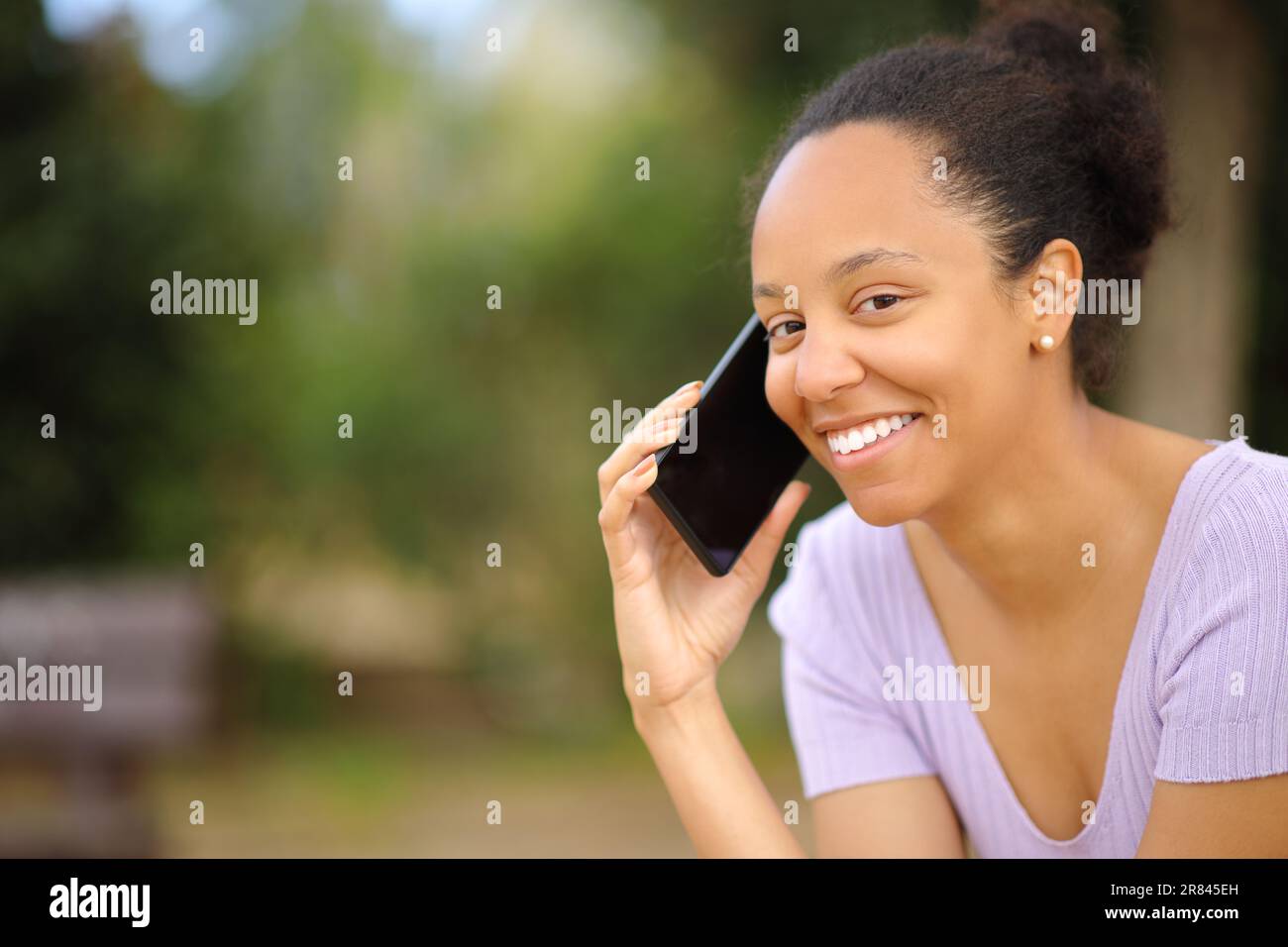 Bonne femme noire qui appelle au téléphone et qui vous regarde dans un parc Banque D'Images