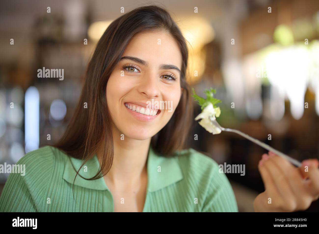 Bonne femme tenant la fourchette avec de la laitue dans un restaurant regardant l'appareil photo Banque D'Images