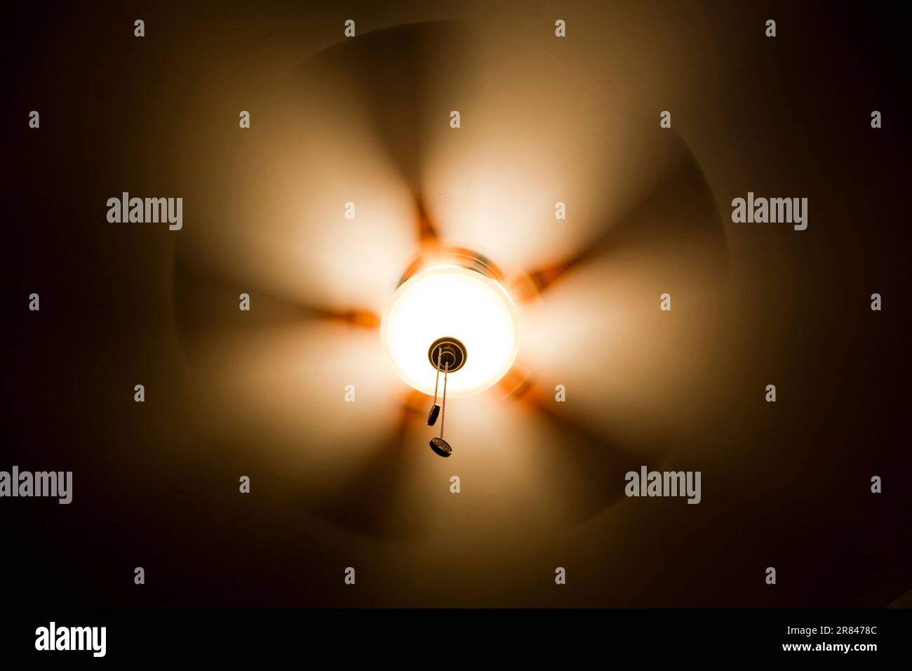 Le mouvement d'un ventilateur de maison illuminé se produit contre le plafond dans une pièce sombre la nuit. Banque D'Images