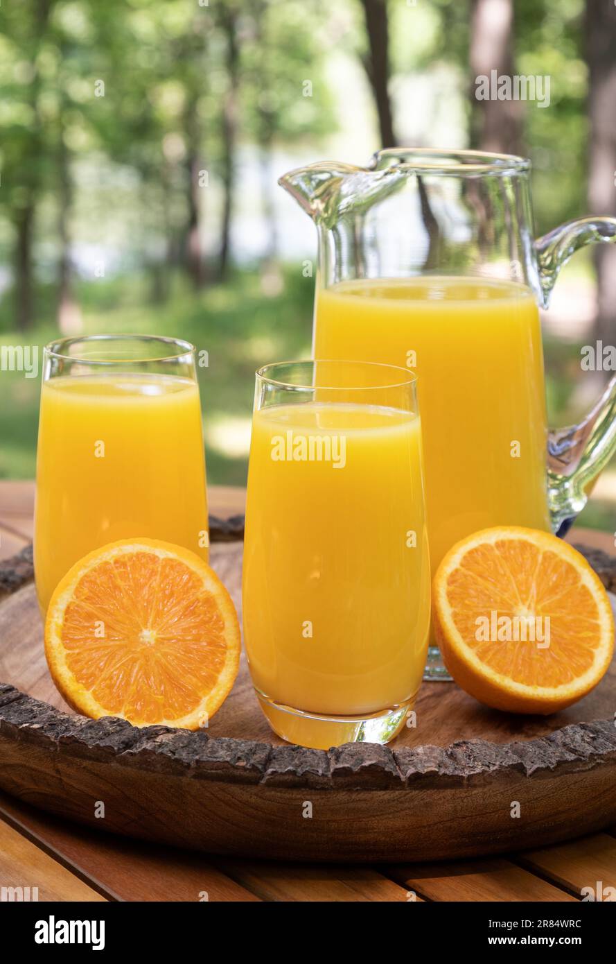 Jus d'orange dans les verres et pither avec des oranges tranchées à l'extérieur sur plateau en bois avec fond de nature Banque D'Images