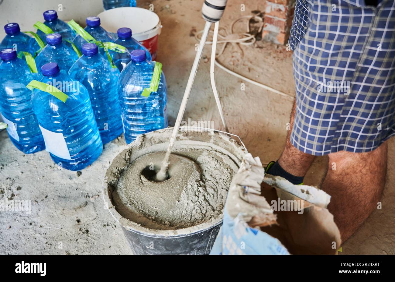 Gros plan de l'homme constructeur dans les gants de travail de préparation du mélange sable-ciment pour briqueter dans le bâtiment en construction. Travailleur masculin mélangeant du mortier avec un mélangeur électrique de ciment pour béton. Banque D'Images