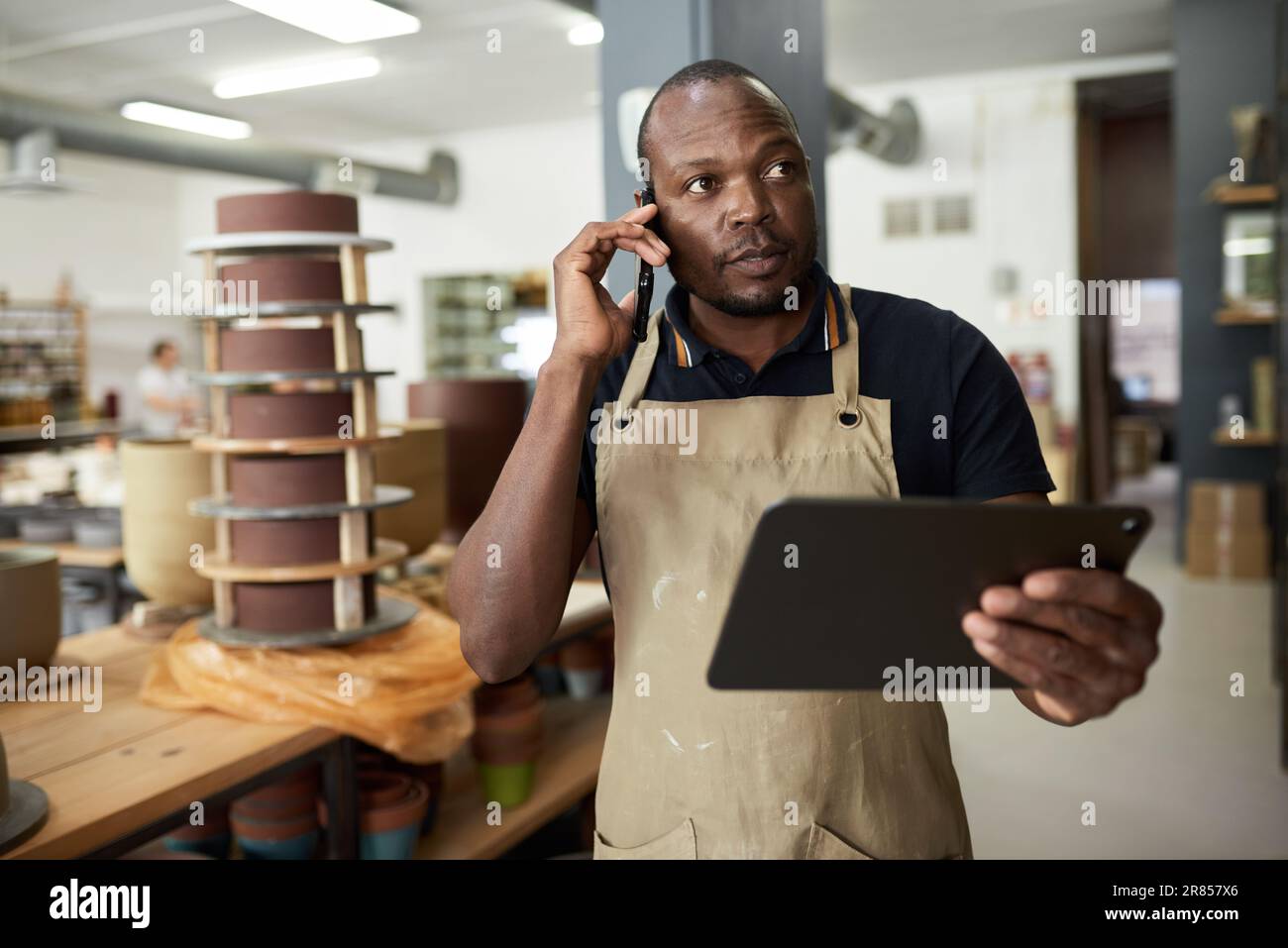 Le directeur du studio de poterie africain parle au téléphone tout en travaillant sur une tablette Banque D'Images