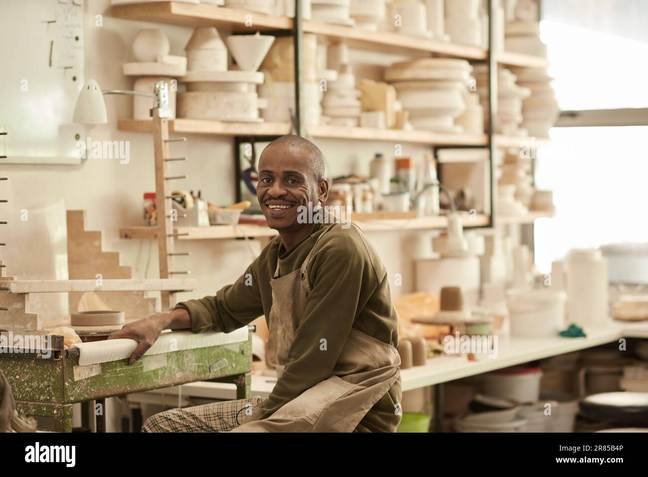 potier africain souriant assis à un banc dans un atelier de poterie Banque D'Images
