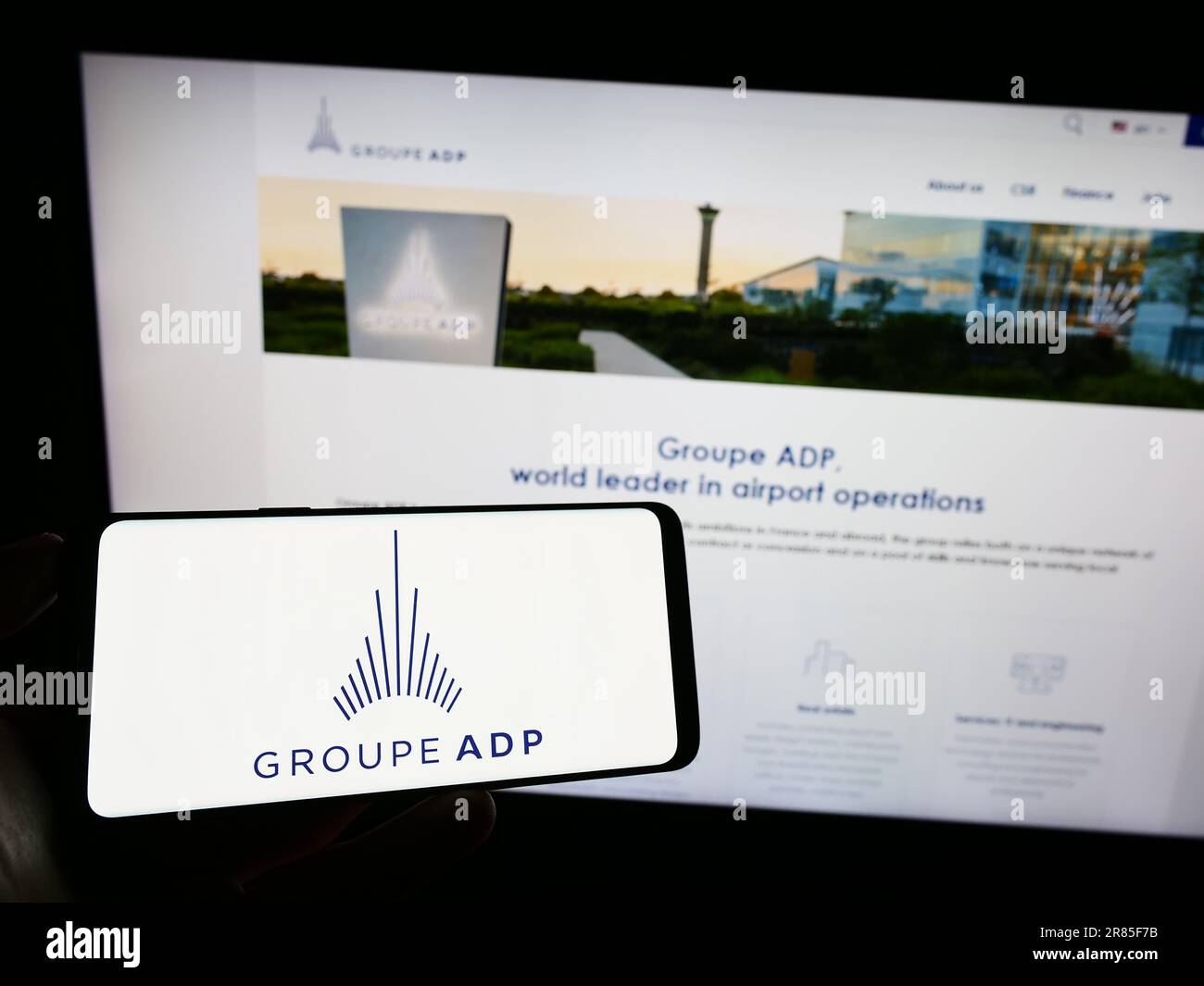 Personne tenant un téléphone portable avec le logo de l'entreprise française d'aérogare Groupe ADP à l'écran en face de la page web. Mise au point sur l'affichage du téléphone. Banque D'Images