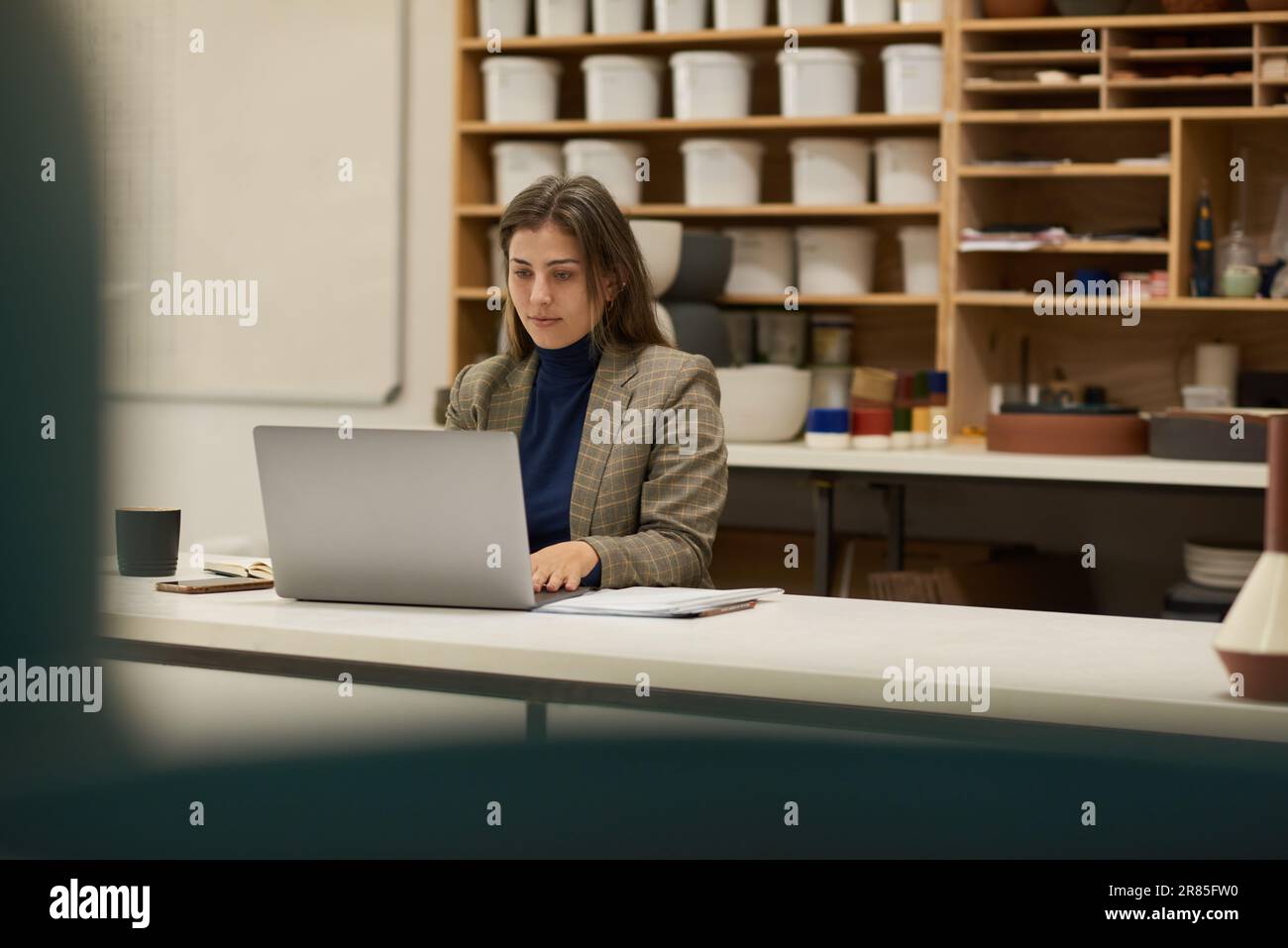 Chef d'atelier céramique travaillant sur un ordinateur portable à une table Banque D'Images