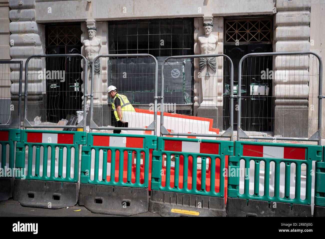 Un ouvrier de la construction fait glisser des barrières au-delà de la façade baroque avec deux figures masculines sculptées au 4 Glasshouse Street, dans le West End, le 19th juin 2023, à Londres, en Angleterre. 4-6 Glasshouse Street Building à Soho, Londres W1. Construit en 1910 pour la London, County & Westminster Bank, le bâtiment qui a été en cours de rénovation a été conçu à l'origine par l'architecte Sir Reginald Blomfield. Banque D'Images